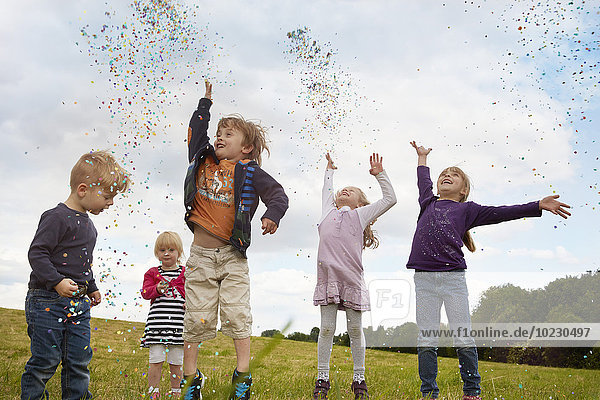 Five little children throwing confetti on a meadow