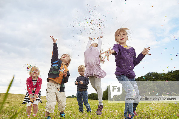 Five little children throwing confetti on a meadow