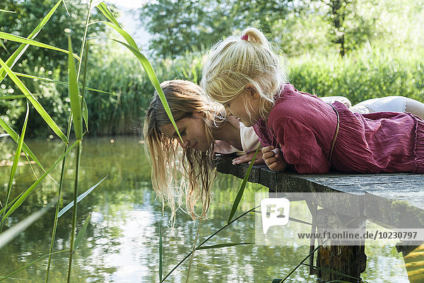 Mother and daughter lying on jetty at a lake looking at water