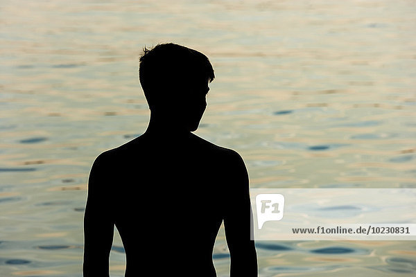 Silhouette eines Teenagers vor einem See bei Dämmerung