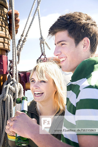 Glücklicher junger Mann und Frau klirrende Bierflaschen auf einem Segelschiff
