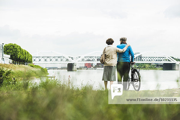 Back view of senior couple standing at water's edge with bicycle