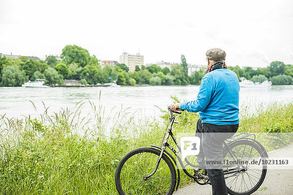 Älterer Mann mit Fahrrad mit Blick auf den Fluss