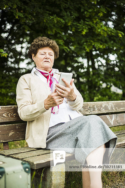 Senior woman sitting on bench using phablet