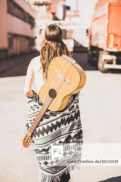 Junge Frau mit Gitarre auf dem Rücken  die auf der Straße geht