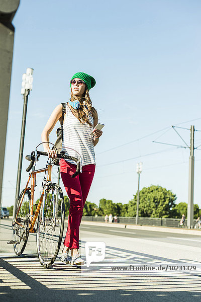 Junge Frau mit Fahrrad auf dem Bürgersteig hält Handy