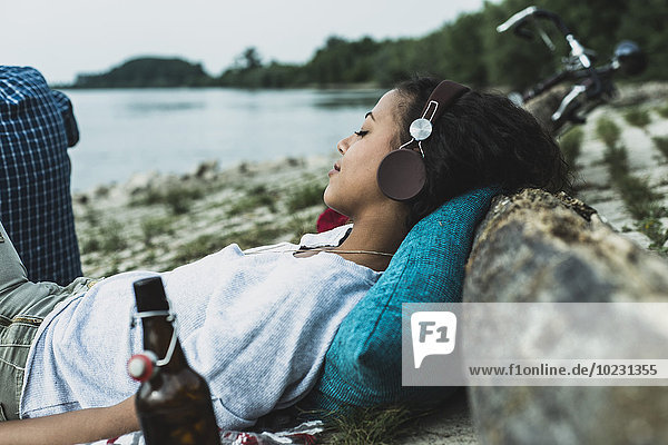 Entspannte junge Frau mit Kopfhörer am Flussufer