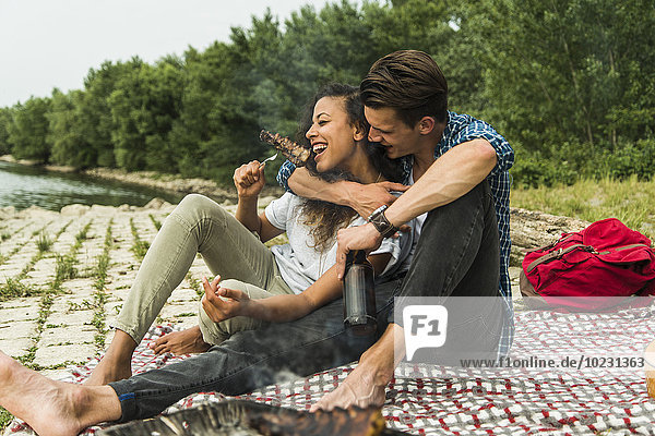 Glückliches junges Paar beim Grillen am Flussufer