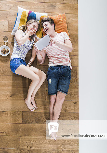 Ein glückliches junges Paar liegt auf dem Boden und teilt sich ein digitales Tablett.