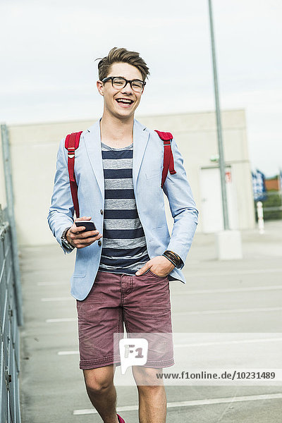 Glücklicher junger Mann  der mit dem Handy im Freien spazieren geht.
