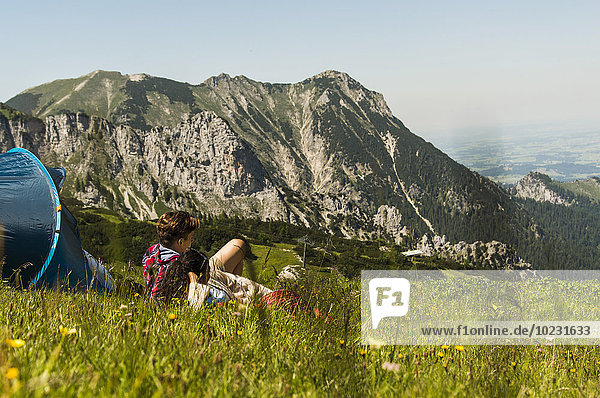 Austria  Tyrol  Tannheimer Tal  young couple resting next to tent on alpine meadow