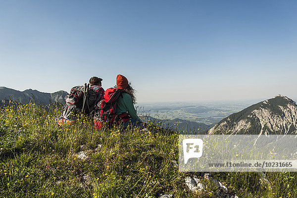 Austria  Tyrol  Tannheimer Tal  young couple sitting on alpine meadow looking at view