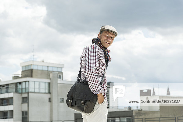 Reifer Mann lächelnd mit Mütze in der Stadt unterwegs