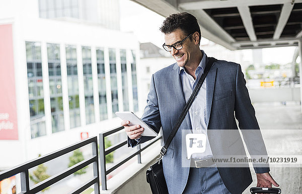 Glücklicher Geschäftsmann auf Geschäftsreise mit Blick auf sein Mini-Tablett