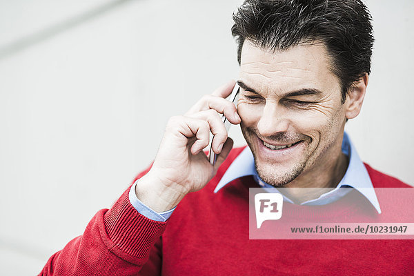 Porträt eines lächelnden Geschäftsmannes mit rotem Pullover telefonieren mit Smartphone