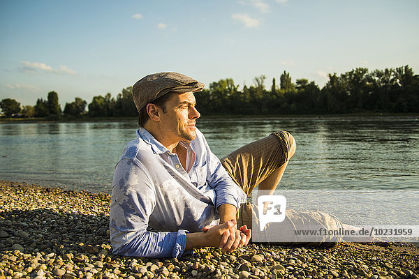 Mann mit Mütze entspannt am Flussufer in der Abenddämmerung