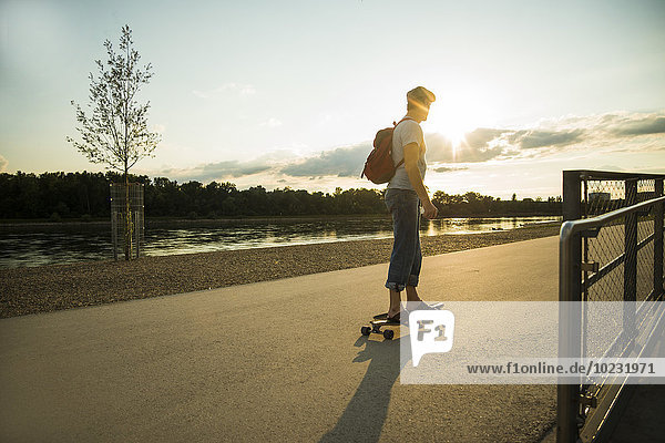 Mann auf dem Skateboard stehend in der Abenddämmerung
