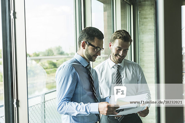 Two young businessmen looking at documents at the window