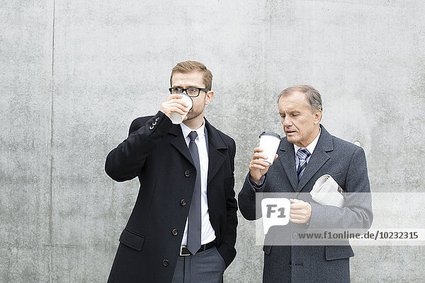 Two businessmen with coffee to go at concrete wall