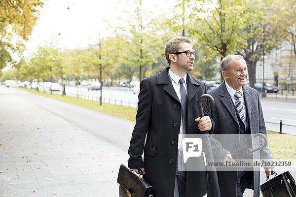Two businessmen walking and talking on pavement