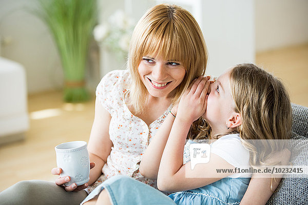 Mother ans daughter sitting on couch with drinking cups