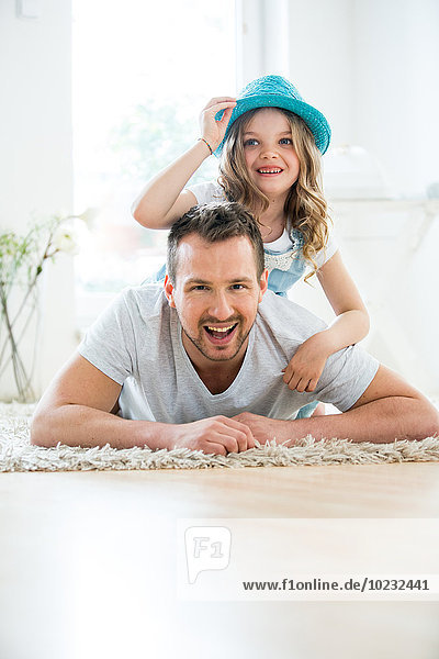 Vater und Tochter auf dem Boden liegend  Mädchen mit Hut spielend