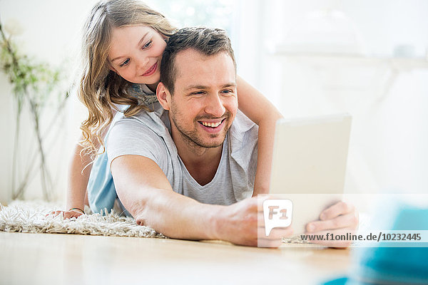 Vater und Tochter auf dem Boden liegend  mit digitalem Tablett