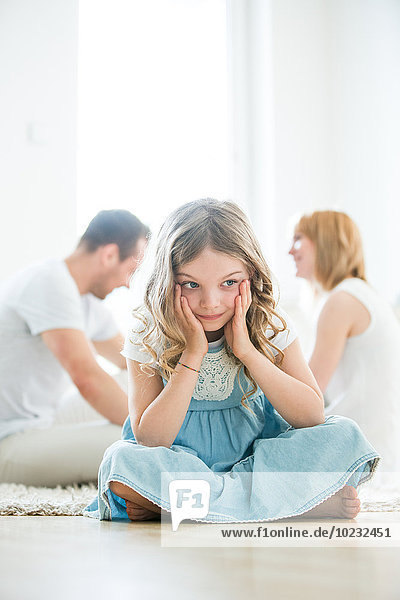 Kleines Mädchen im Schneidersitz auf dem Boden  Eltern sprechen im Hintergrund