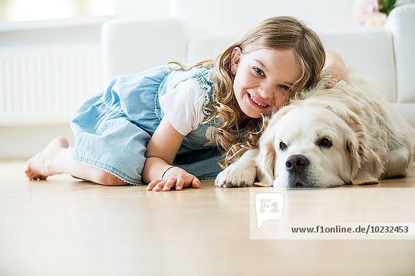 Kleines Mädchen kuschelt mit ihrem Hund  auf dem Boden liegend