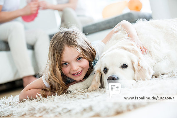 Little girl cuddling with her dog  lying on floor  parents in background