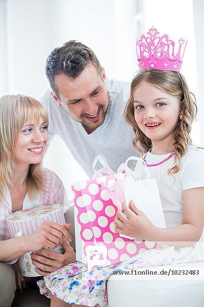 Mädchen in rosa Krone mit Geschenktüten  Eltern schauen zu