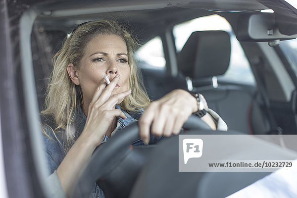 Ernsthafte Frau im Auto  die eine Zigarette raucht.