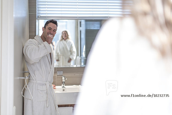 Mann beim Zähneputzen im Hotelbad  während seine Frau ihn beobachtet.