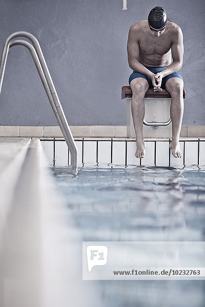 Schwimmer im Hallenbad auf dem Startblock sitzend