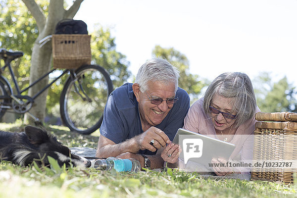 Seniorenpaar liegt auf einer Wiese und schaut auf ein digitales Tablett.