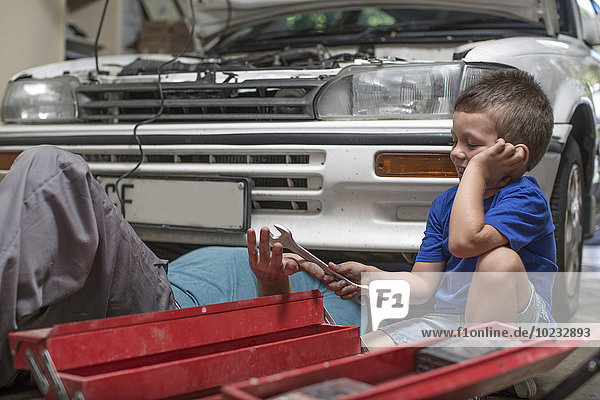 Sohn hilft Vater in der heimischen Garage bei der Arbeit am Auto
