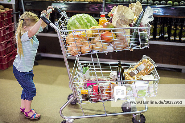 Kleines Mädchen schiebt vollen Einkaufswagen