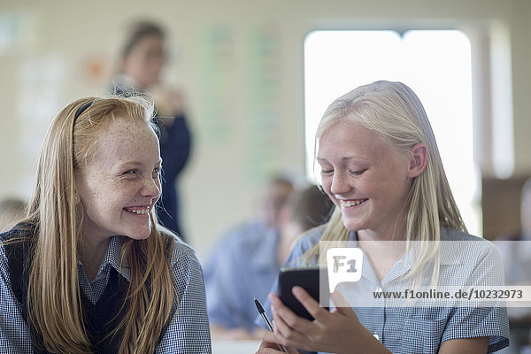 Zwei lächelnde Schülerinnen im Klassenzimmer mit Handy