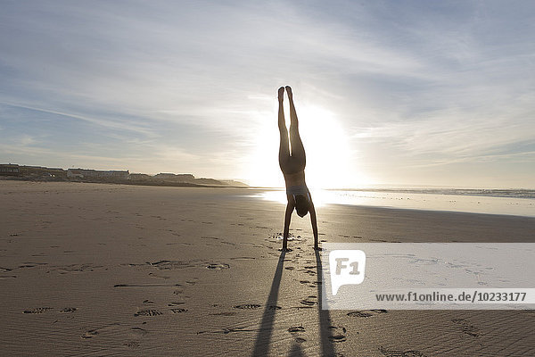 Südafrika  Kapstadt  Silhouette einer jungen Frau beim Handstand am Strand