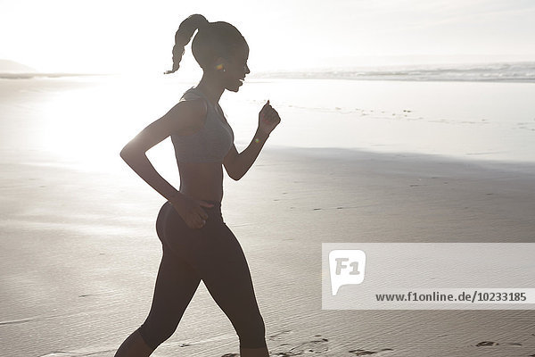 Südafrika  Kapstadt  Silhouette der jungen Frau beim Joggen am Strand
