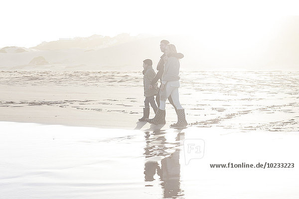 Südafrika  Kapstadt  junges Paar und Sohn beim Spaziergang am Strand im Gegenlicht
