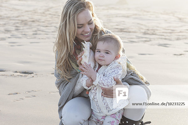 Mutter und kleines Mädchen mit Muschel am Strand