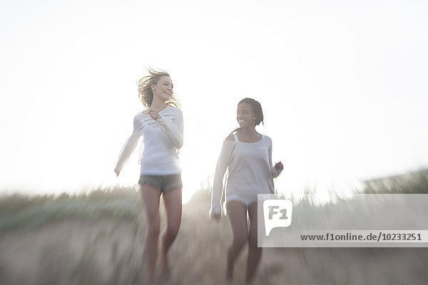 Two female friends running on a beach dune