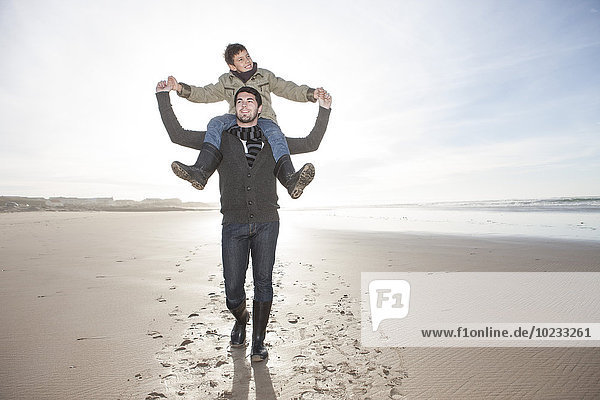 Südafrika  Witsand  Vater trägt seinen Sohn auf den Schultern  während er am Strand spazieren geht.