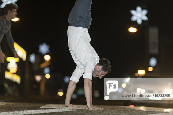 Young man walking on his hands on pavement at night