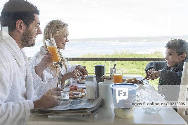 Familie auf der Terrasse des Strandhauses beim Frühstücken