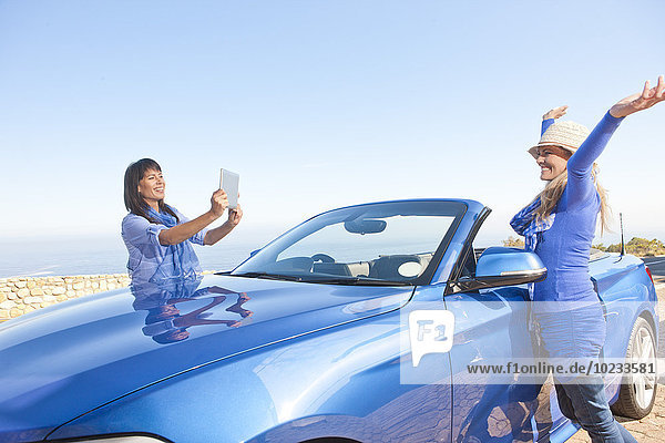 Südafrika  zwei glückliche Frauen bei einem Cabriolet beim Fotografieren mit einem digitalen Tablett