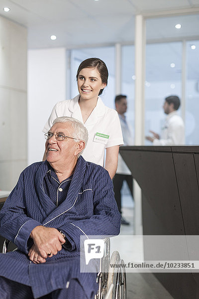 Krankenschwester mit Patient im Rollstuhl an der Klinikrezeption
