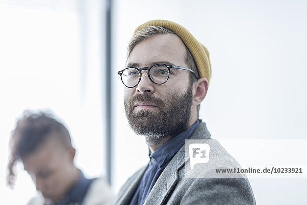 Man with glasses and yellow beanie in meeting with collegues