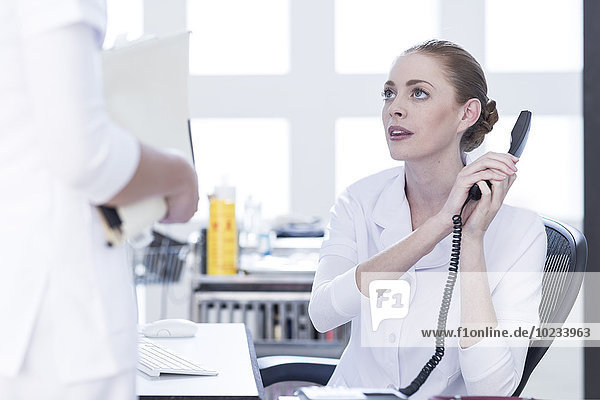 Nurse at desk on the phone looking at doctor